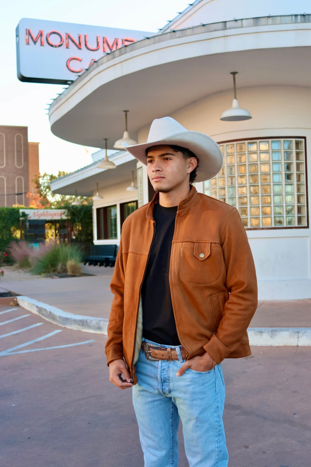 Man wearing a piedreros white/cream cowboy hat, brown jacket, black shirt, and leather belt.