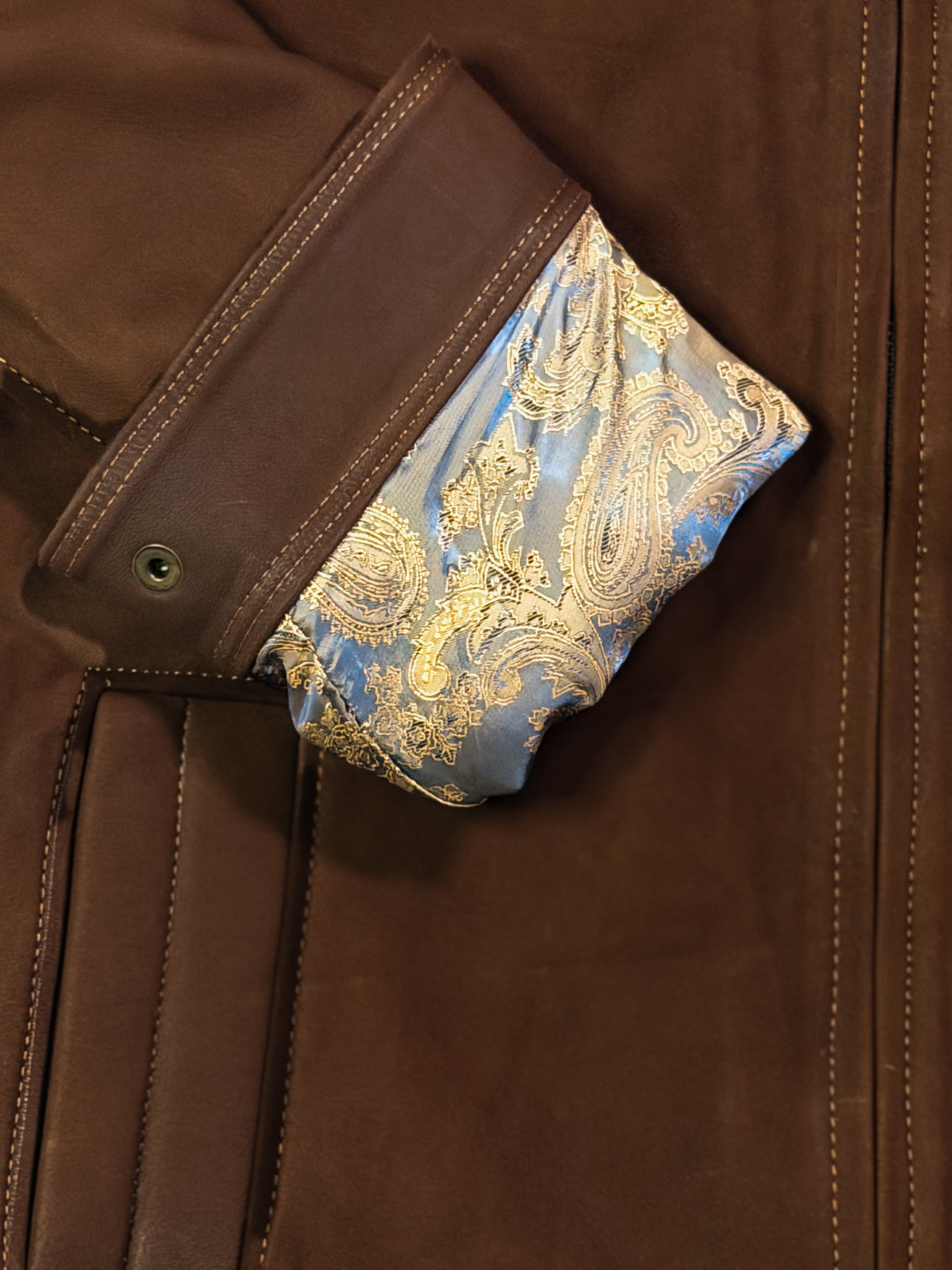 Close-up of a brown leather jacket with a decorative blue and gold inner sleeve.