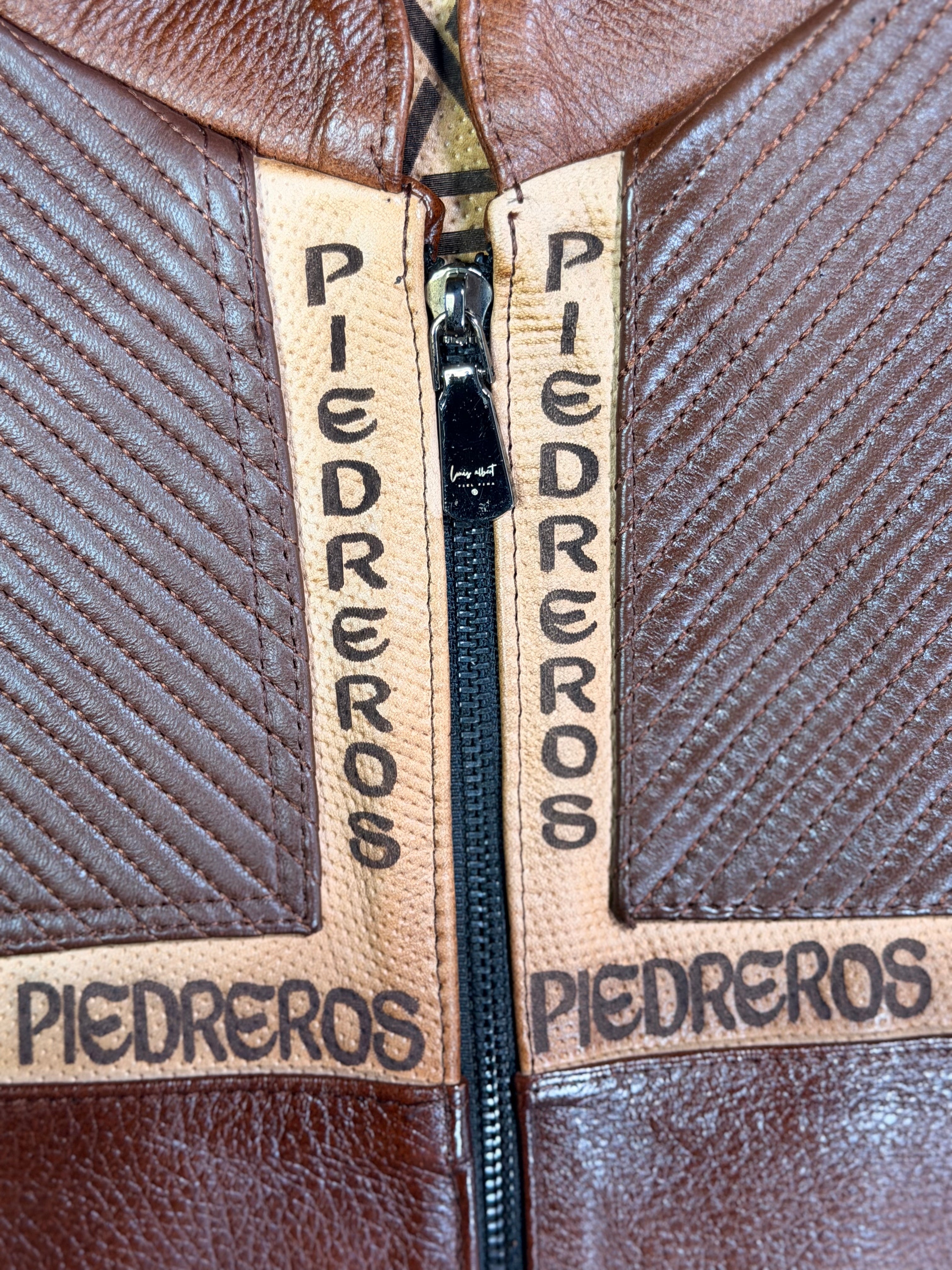 Close-up of a brown leather bag with 'Piedreros' branding on the zipper.