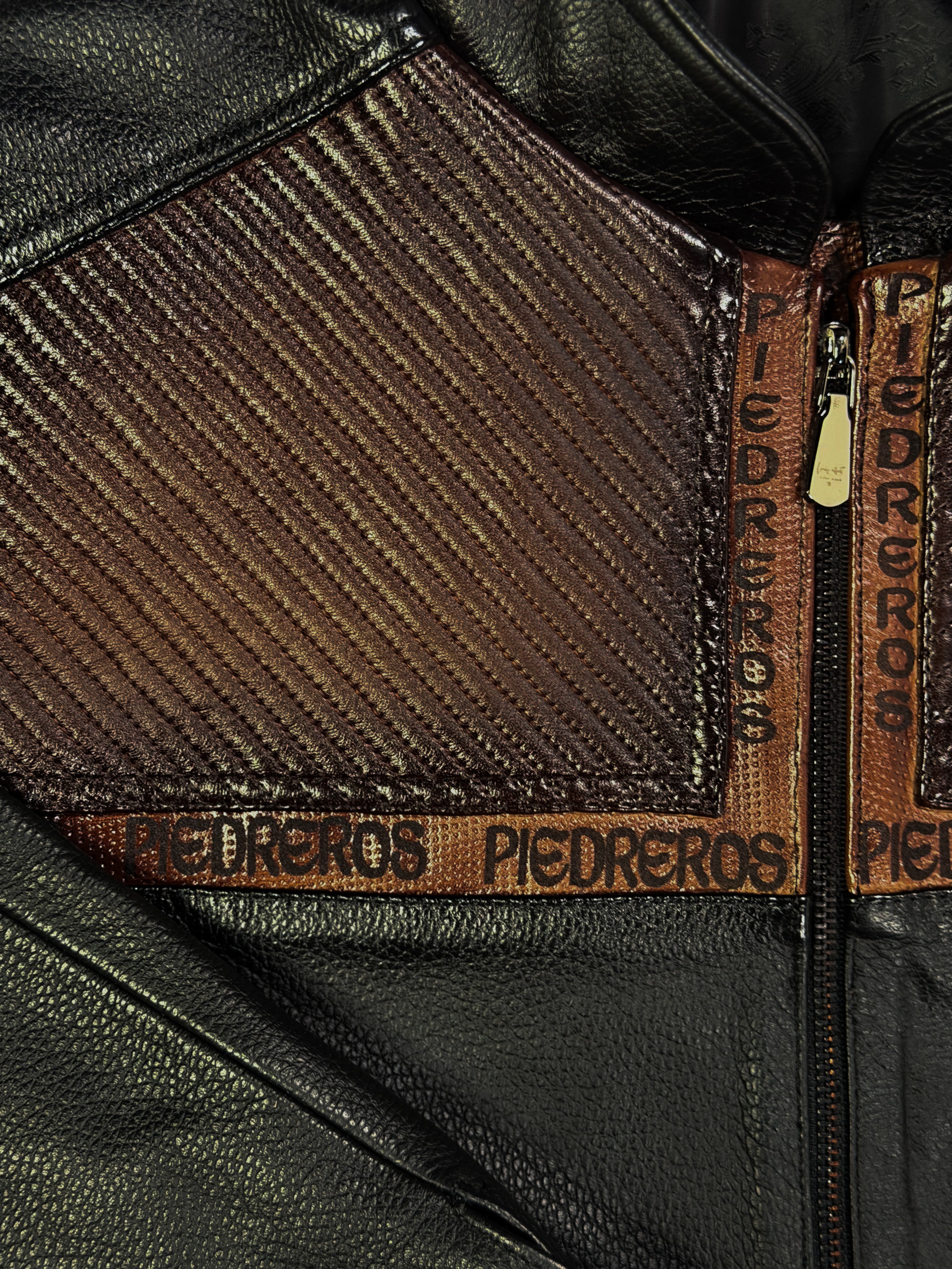 Close-up of the black leather jacket with brown fabric and 'Piedreros' branding.