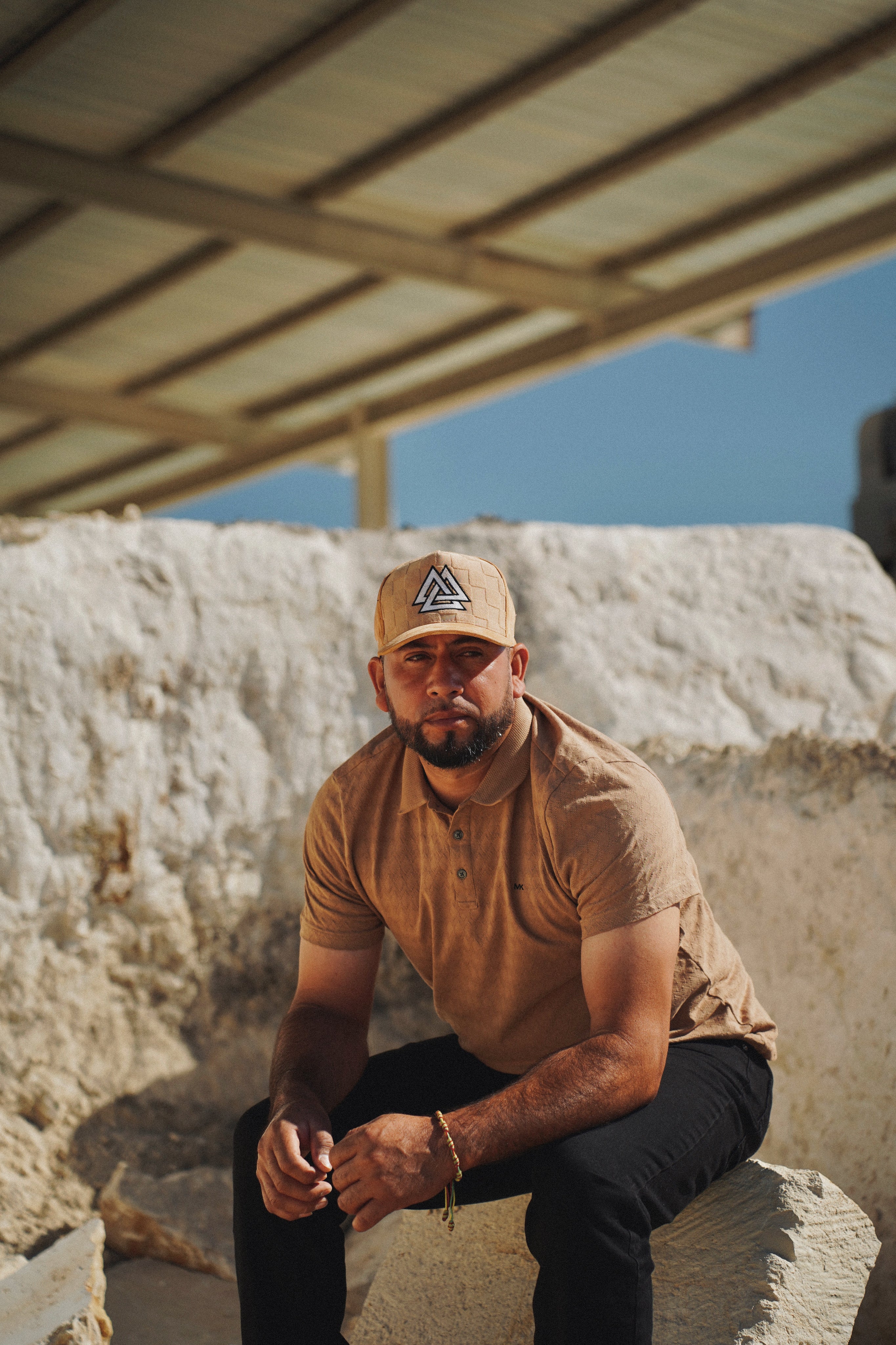 Hombre con la Suede Tri Figure Mesh Cap en gamuza tan, sentado en cantera estilo Cobra Stone, Georgetown TX