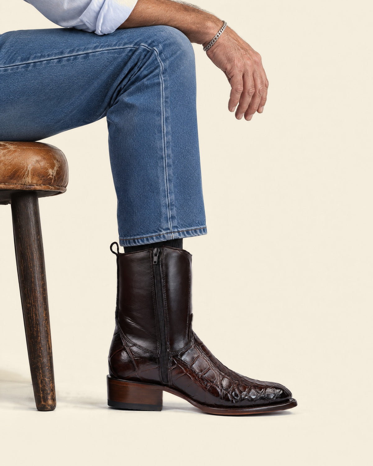 The Zapata in Brown — seated on a leather stool, worn with medium wash jeans